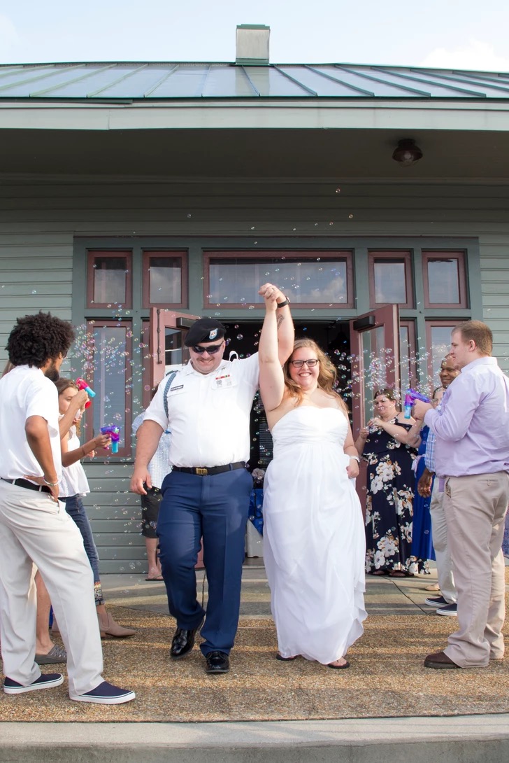 Bride and groom celebrating their exit as guests blow bubbles, groom in military uniform